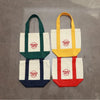 Three canvas bags in green, yellow, and red with white trim displayed on a gray surface.