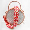 A pink leather crossbody bag with a red and white patterned strap.