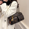 A woman holds a dark brown vintage letter print crossbody bag against a white coat.