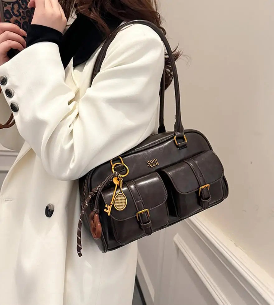 A woman holds a dark brown vintage letter print crossbody bag against a white coat.