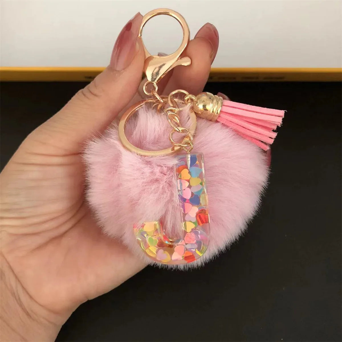 A hand holds a custom initial letter keychain featuring a shiny resin pendant and pink alphabet charm.