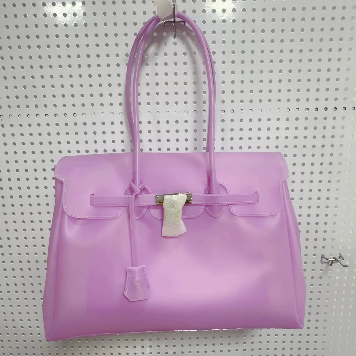 Helles lila Sommer-Gelidertasche mit Henkel und silberner Hardware vor gepunktetem Hintergrund.