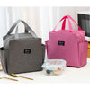 A pink insulated canvas tote bag with double pockets sits on a white surface next to a clear plastic container.