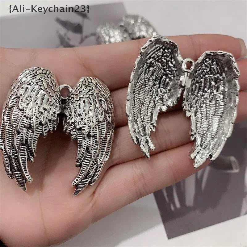 Silver metal angel wing keychain charm displayed on a hand.