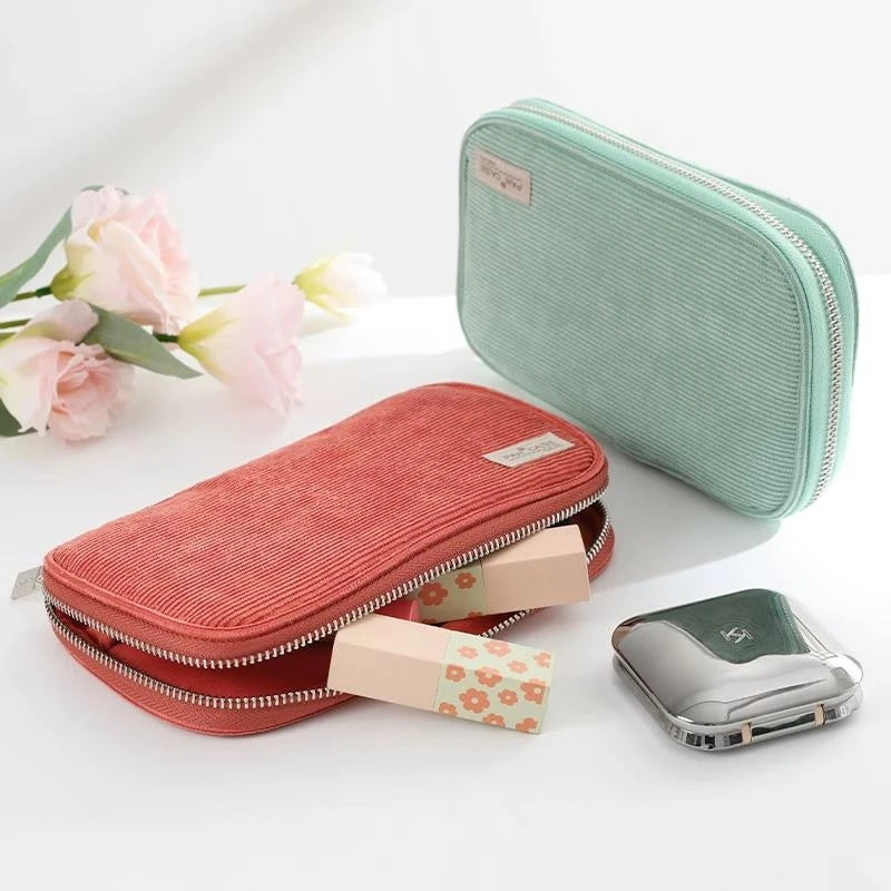 A pink corduroy pencil case with a fold-out tray and a silver metal accessory shown next to it.
