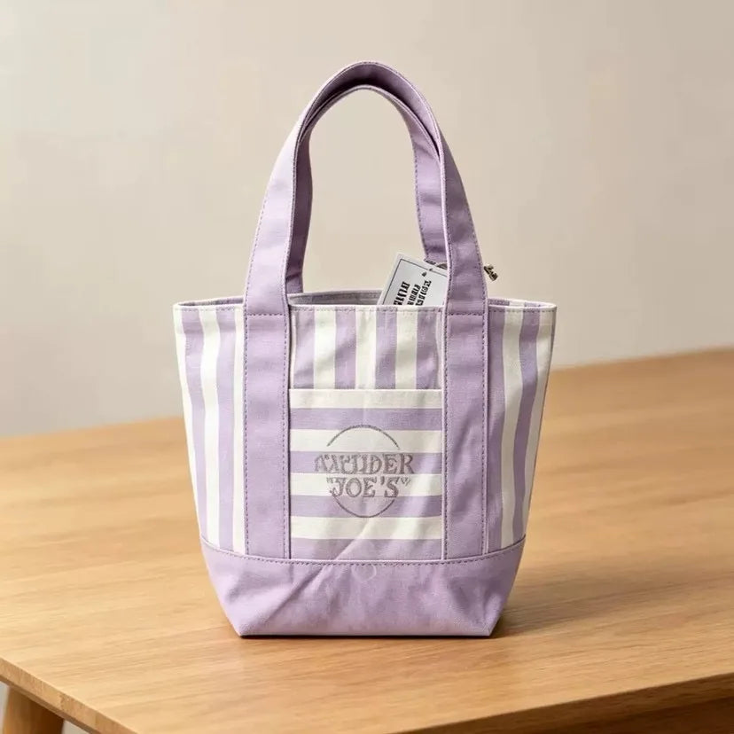 Una bolsa de lona a rayas moradas y blancas con asa sobre una superficie de madera.