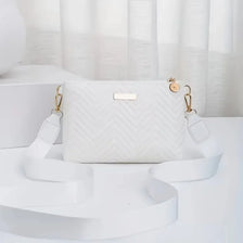 A white quilted crossbody bag with gold hardware resting on a white surface.