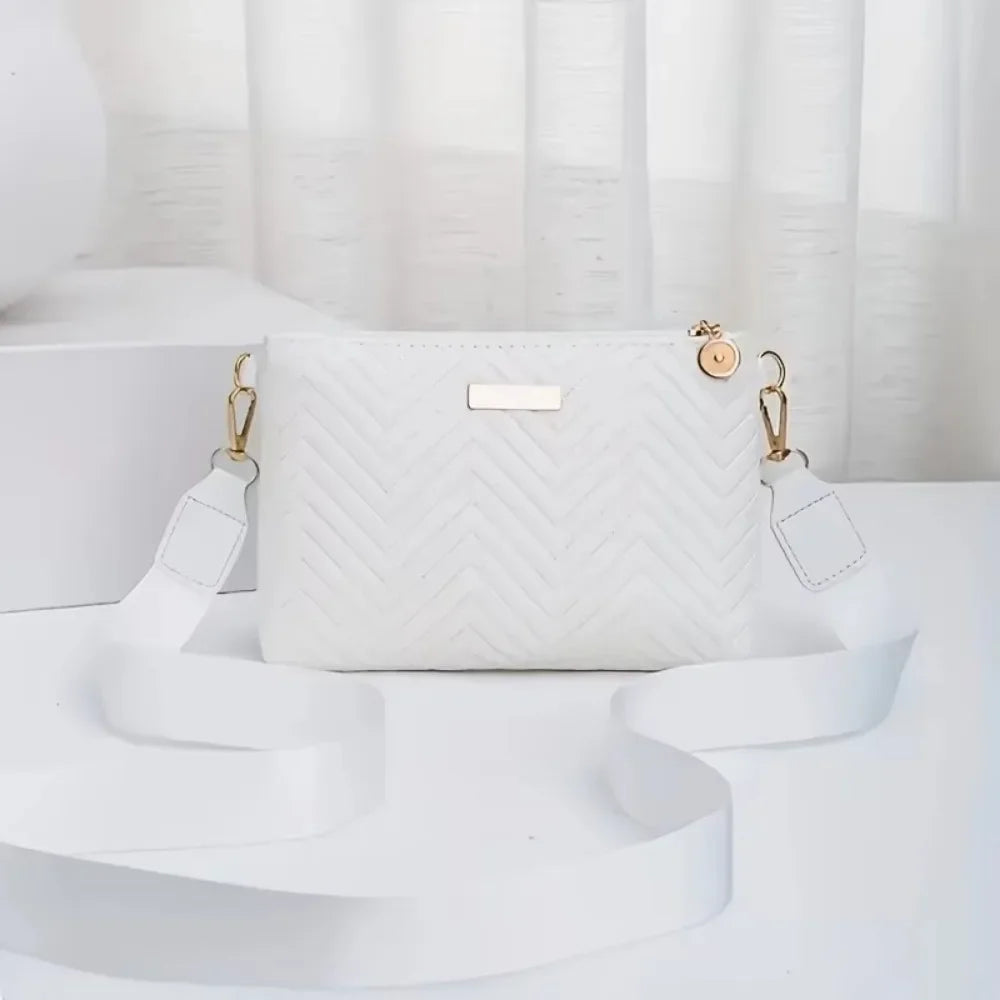 A white quilted crossbody bag with gold hardware resting on a white surface.