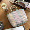 A light pink and green hand woven PVC vegetable basket tote bag resting on a wooden table.