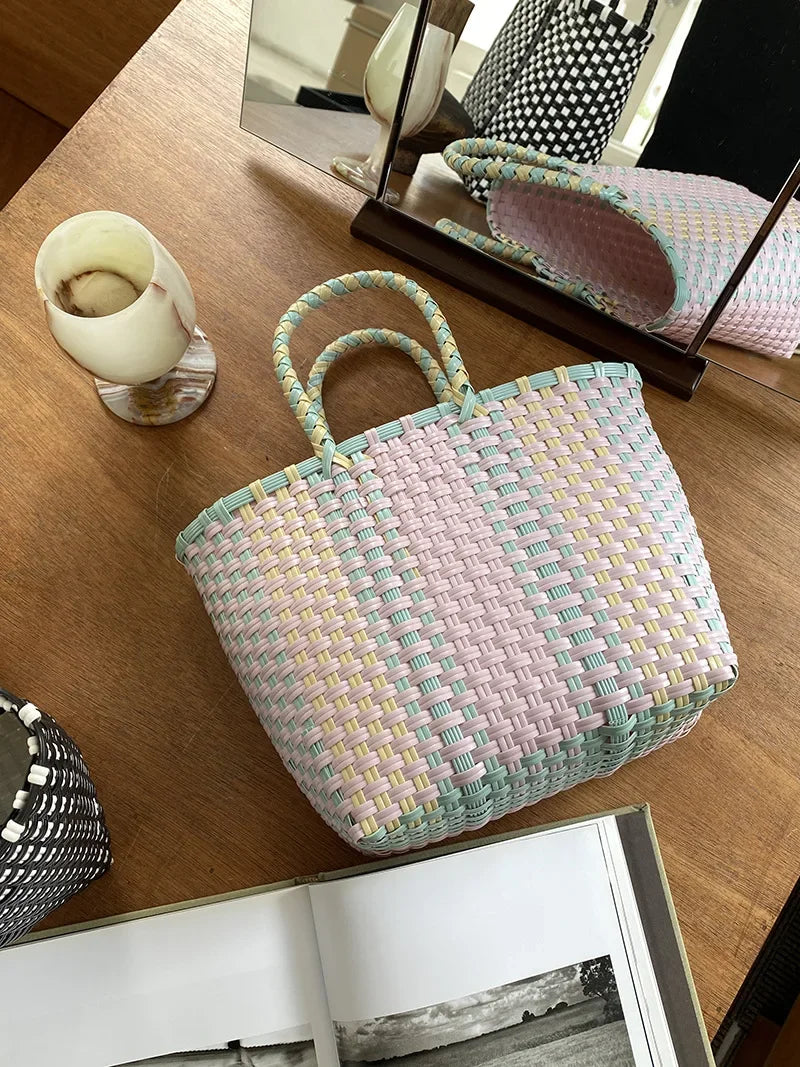 A light pink and green hand woven PVC vegetable basket tote bag resting on a wooden table.