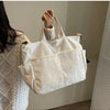 A white corduroy multi-pocket tote bag is hanging on a door, held by a person's hand.
