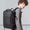 A man wearing a grey coat is holding a black men's business travel backpack.
