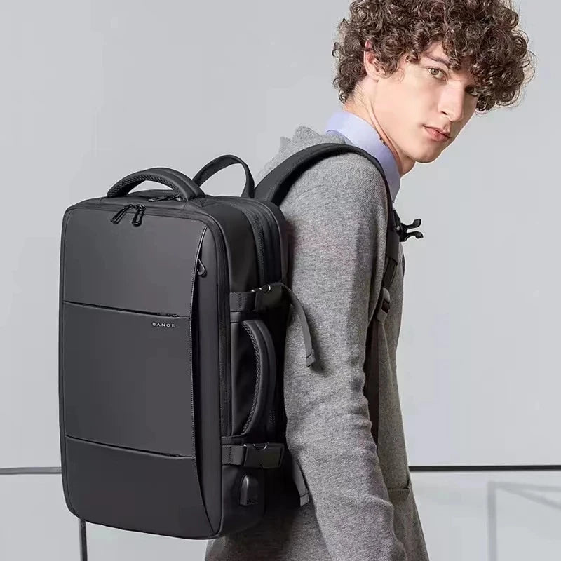 A man wearing a grey coat is holding a black men's business travel backpack.