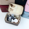 A gray makeup bag with compartments holds various cosmetic tools and products like brushes and jars.