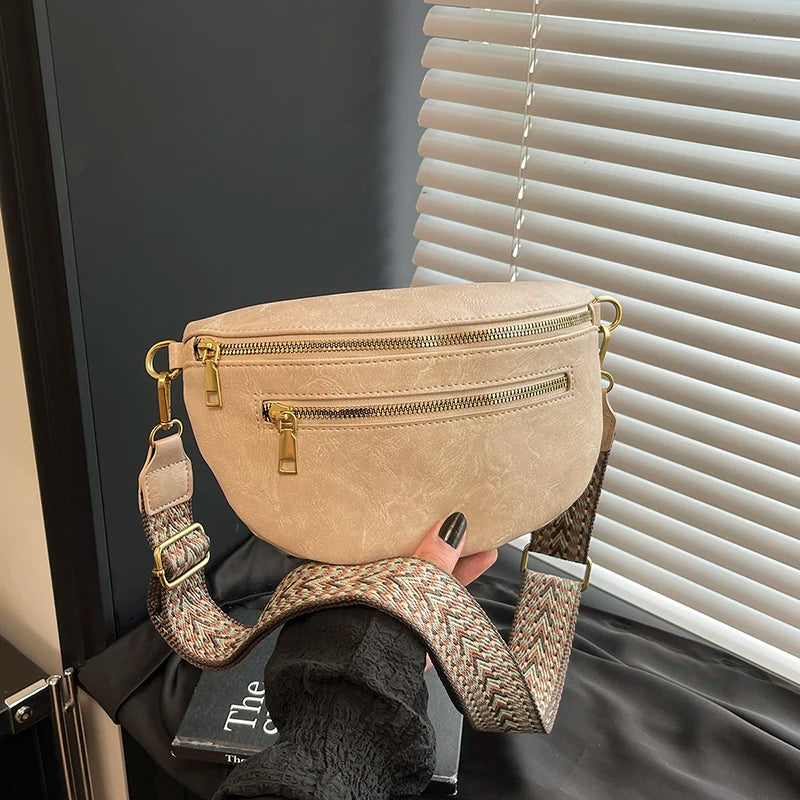 A beige PU leather crossbody bag with a gold-toned adjustable strap is held against a window blind.