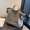 A grey canvas tote bag with tan handles is displayed on a dark surface.