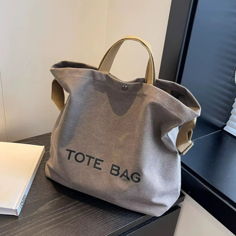 A grey canvas tote bag with tan handles is displayed on a dark surface.