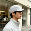 A young man wearing a light gray mesh baseball cap and a white jacket stands in front of a glass storefront.