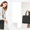 A woman holds a black premium PU leather laptop tote bag in a light beige blazer.