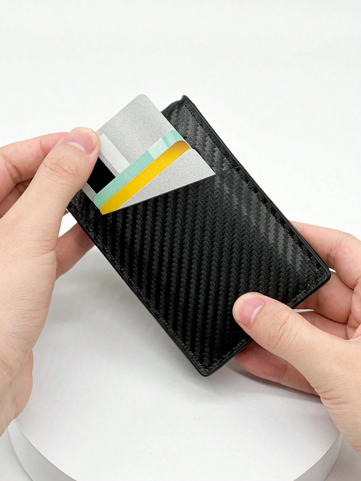 Una mano sostiene un estuche para tarjetas de fibra de carbono negra con una tarjeta plateada y verde azulada dentro.
