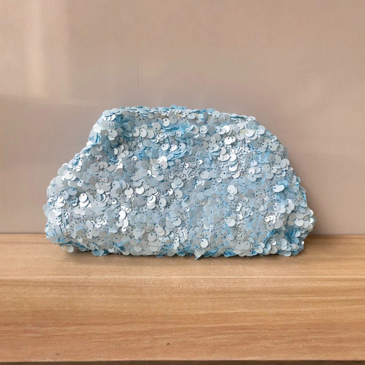 A light blue beaded chain shoulder clutch bag resting on a wooden surface.