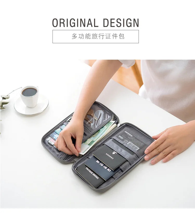 A hand is opening a dark gray multi-pocket travel document organizer filled with various currency and documents on a white ta
