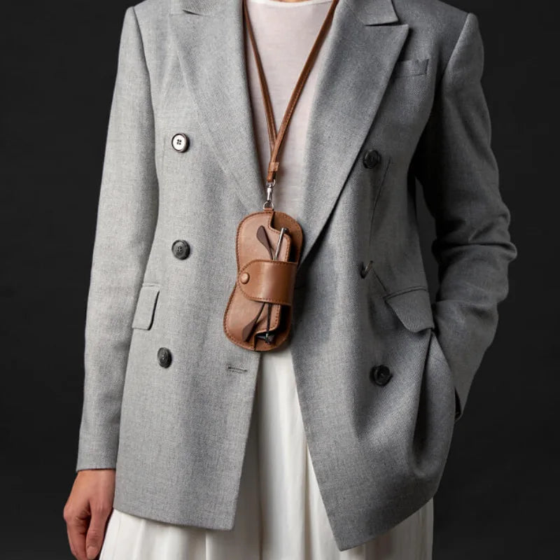 A gray blazer worn over a white top, featuring a brown leather lariat necklace and storage case.