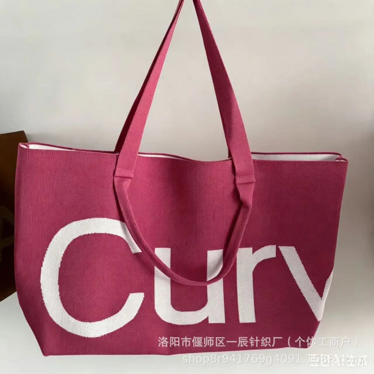 A pink knitted large tote bag with a white logo featuring the word curvy