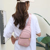 Eine Frau trägt ein weißes T-Shirt und eine rosa Baseballkappe und hält eine pinke gesteppte wasserdichte Crossbody-Tasche.