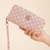 A hand holds a pink monogrammed wallet with a zipper pull against a light background.