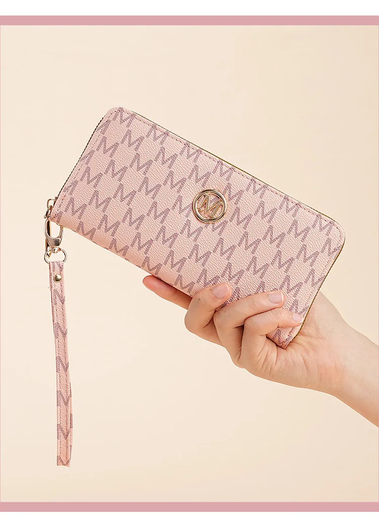 A hand holds a pink monogrammed wallet with a zipper pull against a light background.