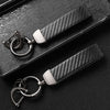 A close-up shot of a black carbon fiber leather keychain resting on a dark surface.