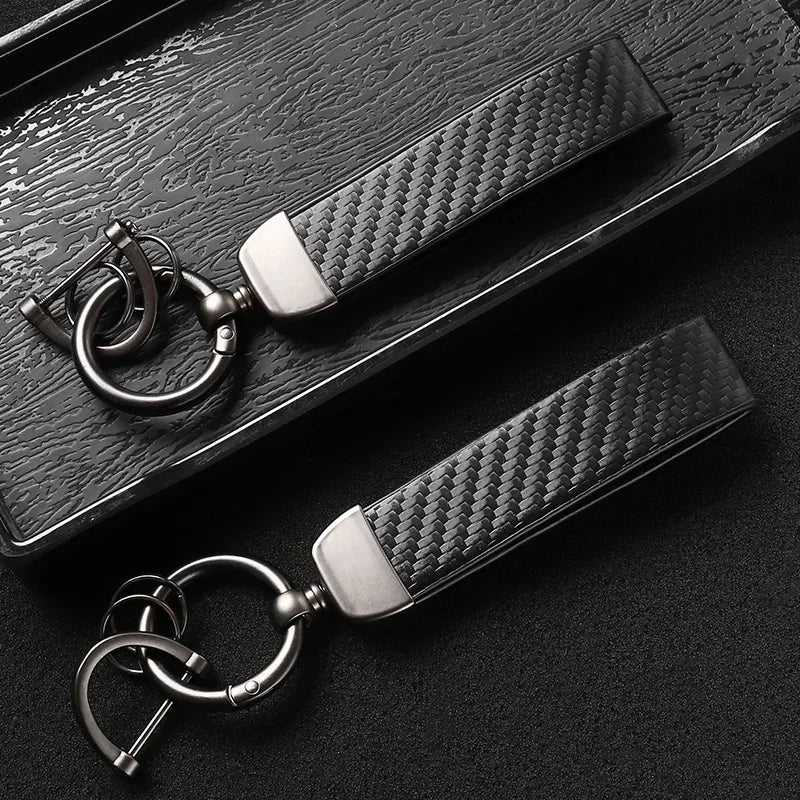 A close-up shot of a black carbon fiber leather keychain resting on a dark surface.