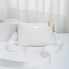 A white quilted leather crossbody bag with gold hardware resting on a white surface.