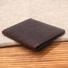 A dark brown genuine leather bifold card holder resting on a beige woven fabric surface.