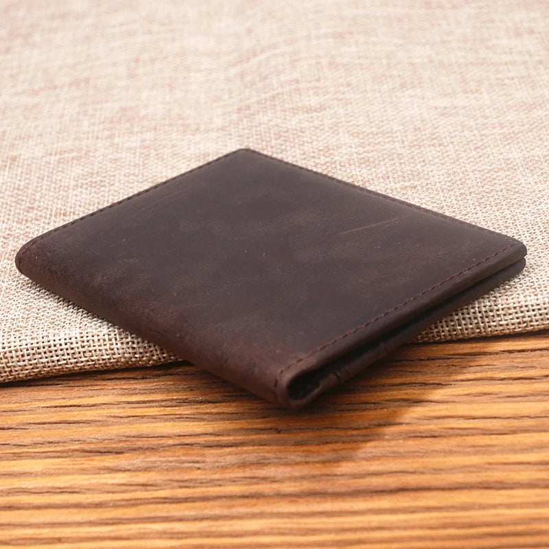A dark brown genuine leather bifold card holder resting on a beige woven fabric surface.