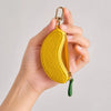 A hand holds a yellow fruit-shaped PU leather coin purse keychain with a gold clasp and green tassel.