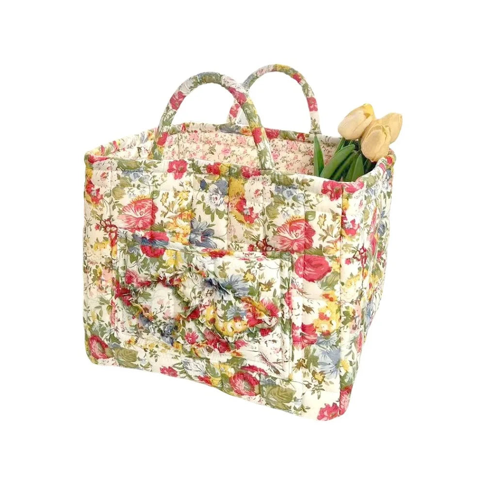 A quilted fabric storage basket with carry handles featuring a floral pattern, holding yellow tulips.