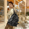 A woman wearing a cream corduroy bow print backpack stands in a bright interior setting.