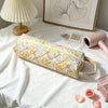 A floral patterned quilting storage bag lying on a white surface next to a lamp and framed art.