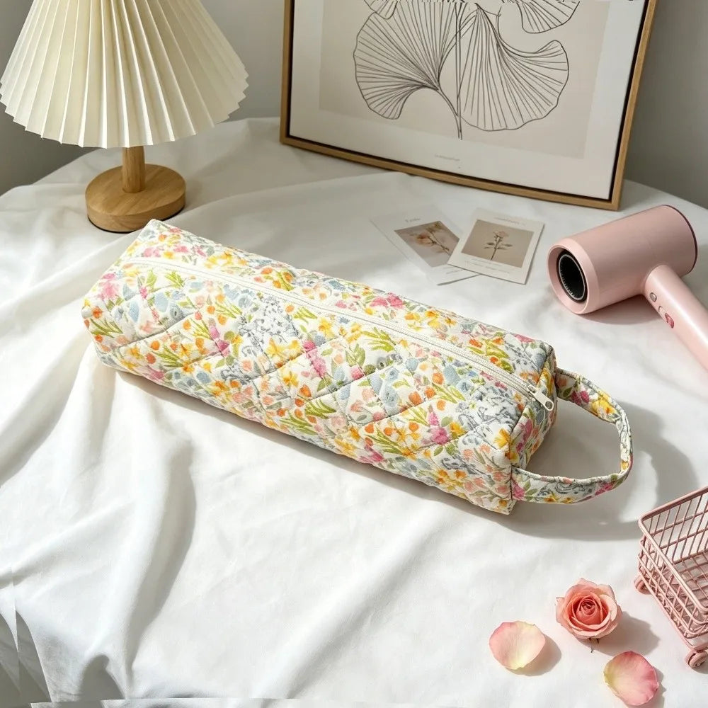 A floral patterned quilting storage bag lying on a white surface next to a lamp and framed art.