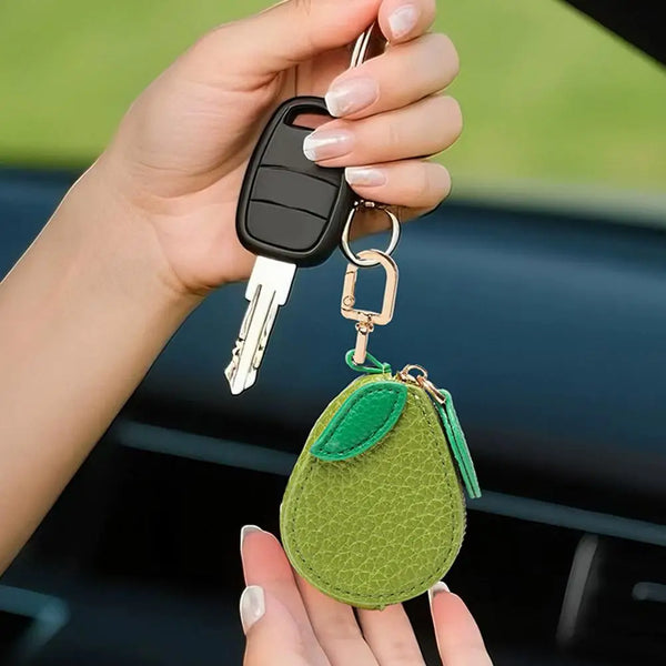 A hand holds a fruit-shaped leather coin purse keychain with a black fob and silver keyring.