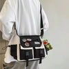 Una persona sostiene un bolso cruzado de nylon blanco y negro con un juguete de peluche verde.