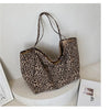 A leopard print canvas crossbody tote bag displayed on a white circular stand.