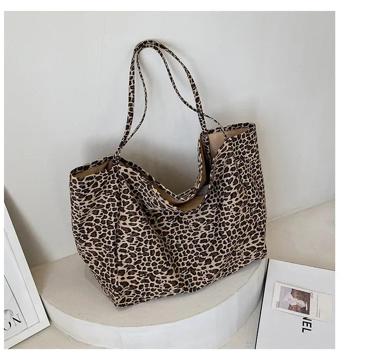 A leopard print canvas crossbody tote bag displayed on a white circular stand.
