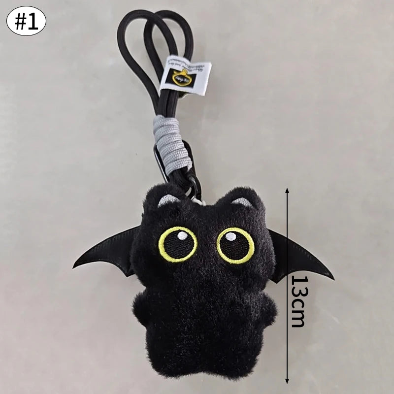 Colgante llavero de peluche de gato negro contra un fondo gris claro.