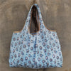 A light blue patterned reusable shopping bag hanging against a gray concrete wall.
