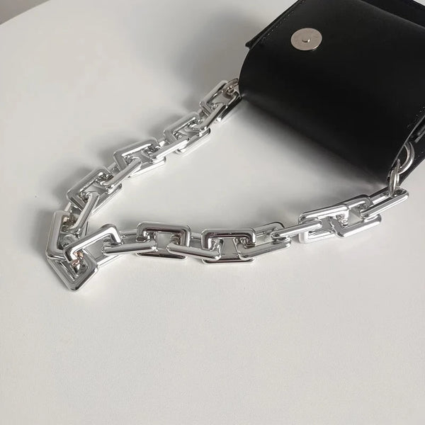 Correa de cadena de acrílico plateado unida a un bolso de cuero negro.
