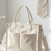 Sac fourre-tout beige en velours côtelé avec des pois roses clairs et une sangle tissée, accroché à un mur blanc.