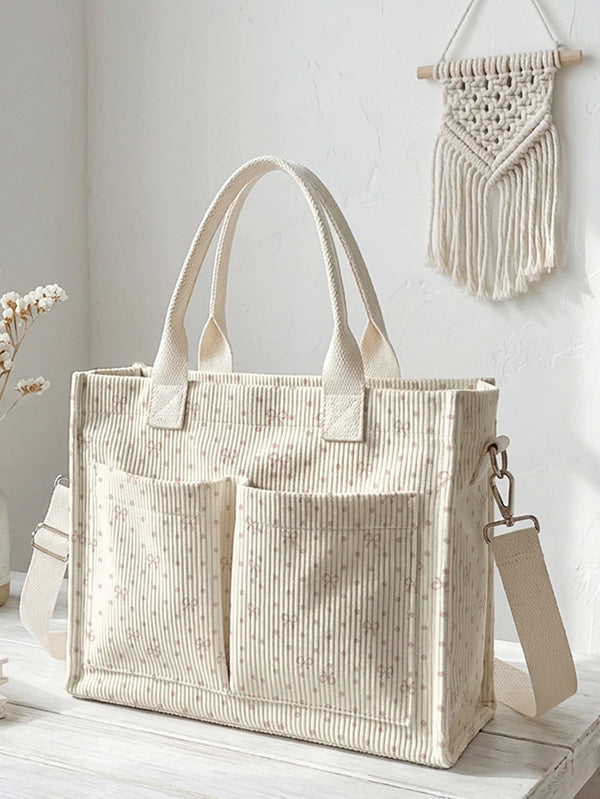 A beige corduroy tote bag with light pink polka dots and a woven strap hanging on a white wall.